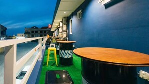 Eine Terrasse mit Tischen und Hocker, einer Geländer und Blick auf Gebäude im Hintergrund.