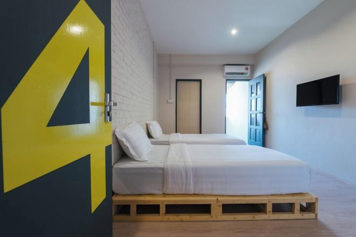 A room with two beds, a door with a large number 4, a TV on the wall, and an air conditioning unit.
