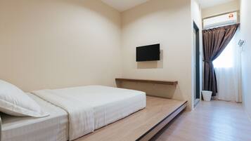 A minimalist bedroom with a single bed, a mounted TV, and a small window with curtains.