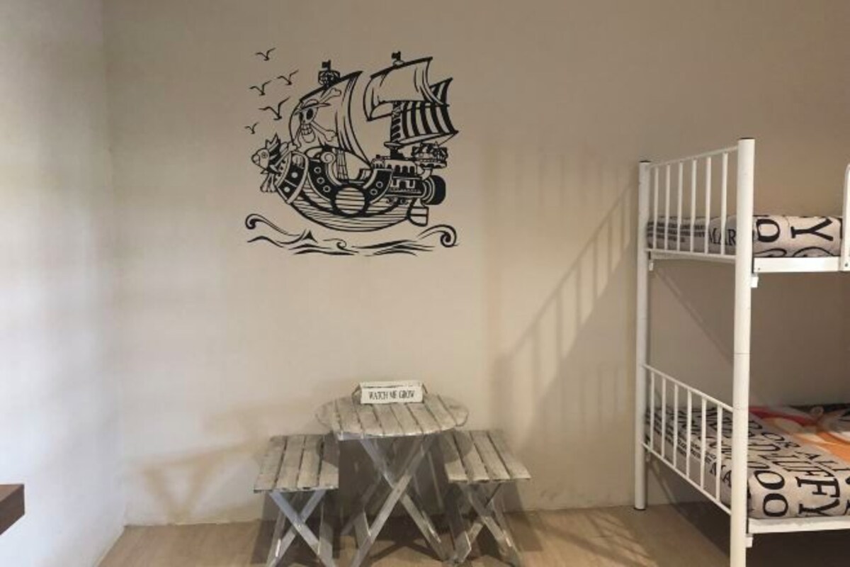 A room with a bunk bed, a small wooden stool, and a wall decal of a ship.