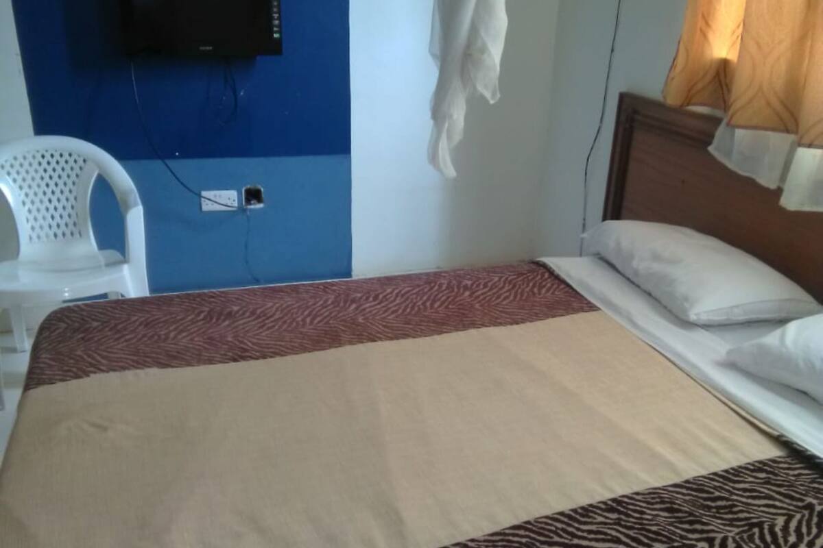 Uma cama com colcha estampada em padrão de zebra, uma cadeira branca, uma televisão fixada numa parede azul e uma janela com cortinas.
