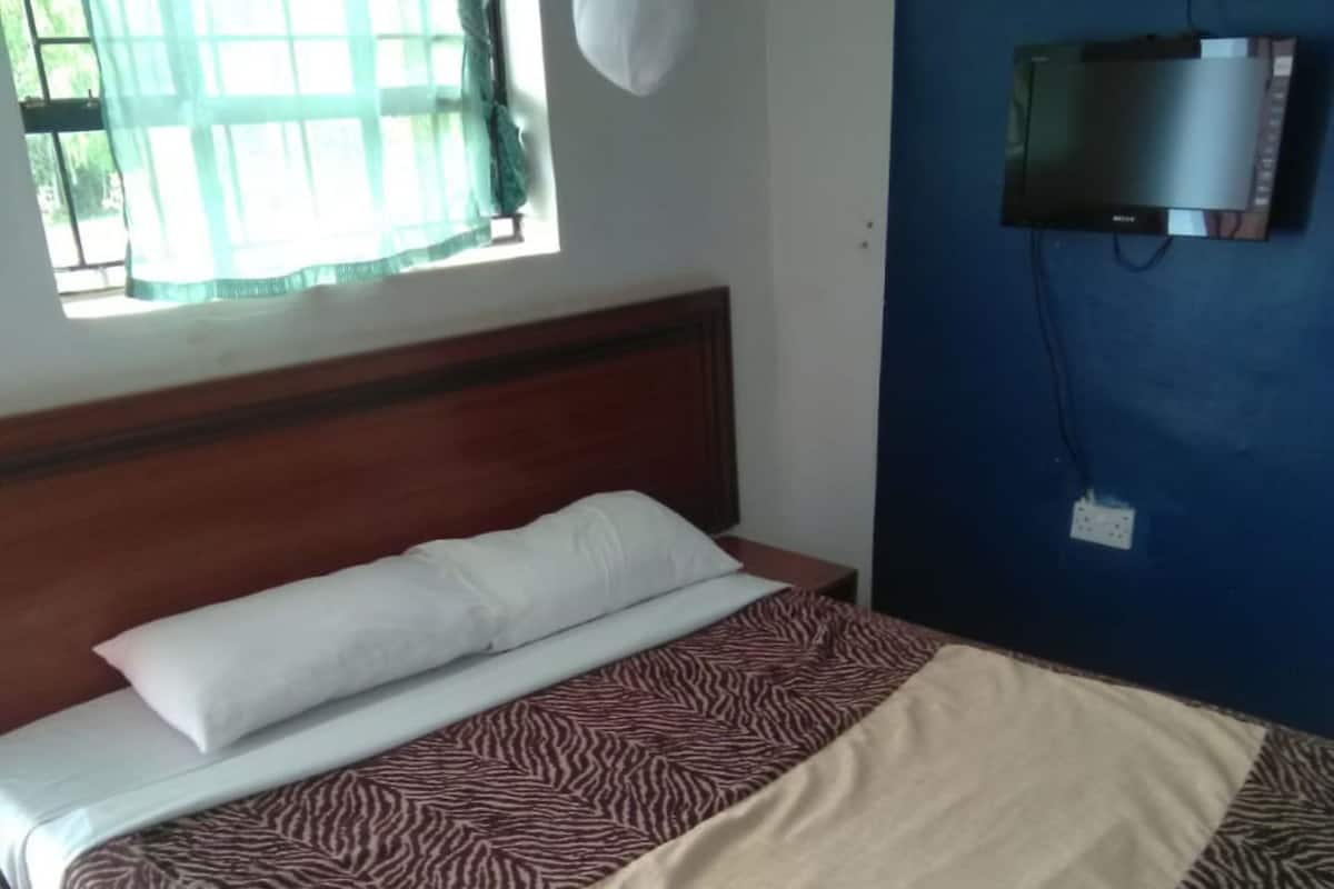 Quarto com cama, televisão na parede e janela com cortinas.