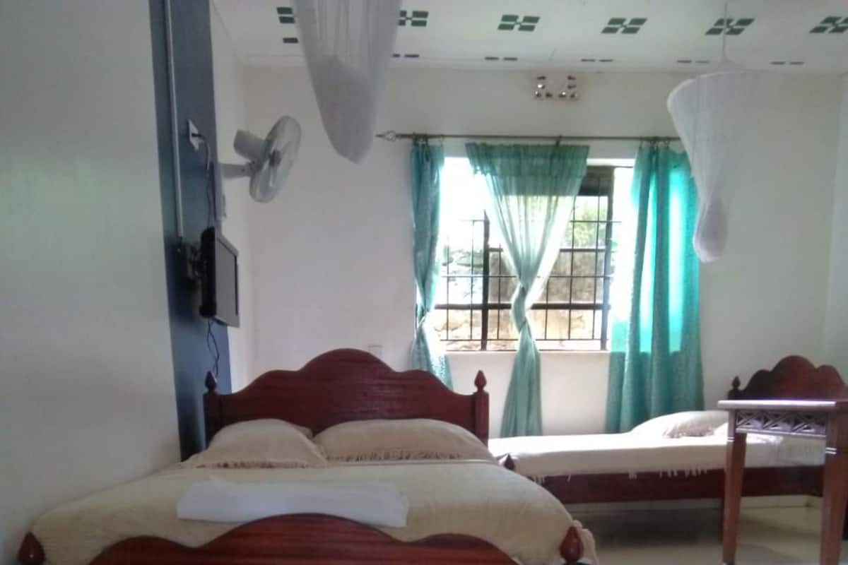 Quarto com cama de madeira, mesa de cabeceira, ventoinha e janela com cortinas.