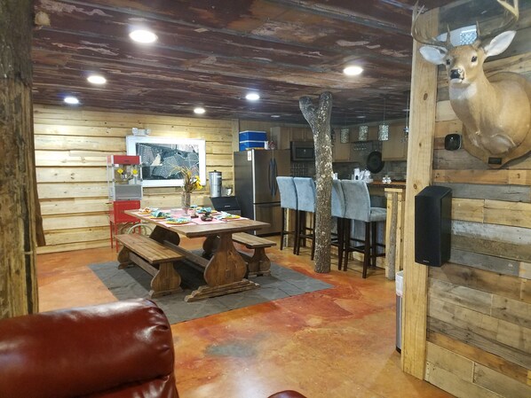 A rustic dining area with a wooden table, benches, and a mounted deer head on the wall. - Red Fern Lodge Room 5 (Statesboro)