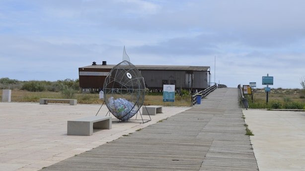 A boardwalk leading to a modern building with a unique spherical sculpture and a signboard.