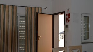 A room with a wooden door, a telephone, a window, and a curtain.