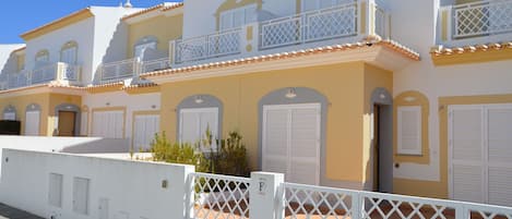 A row of yellow buildings with white balconies and shutters.
