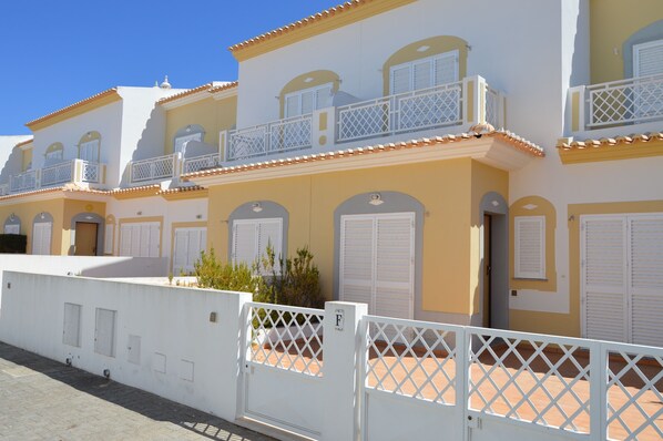 A row of yellow buildings with white balconies and shutters.
