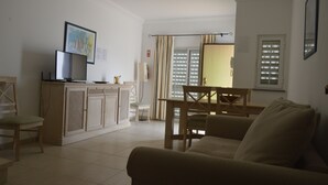 A living room with a sofa, a dining table with chairs, a TV on a stand, and a cabinet.