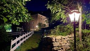 Un bâtiment en pierre, avec une clôture blanche et un mur de pierre, entouré de verdure.