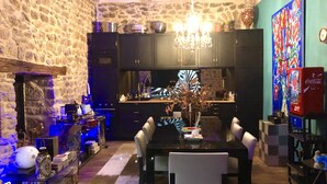 Un coin repas chaleureux avec un mur en pierre, un lustre et une cuisine moderne en arrière-plan.