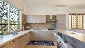 Una cocina moderna con armarios de madera clara, salpicadero de piedra y un amplio ventanal con diseño de celosía.
