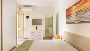 Un dormitorio con cama, cómoda, espejo y un cuadro de un atardecer sobre el océano.