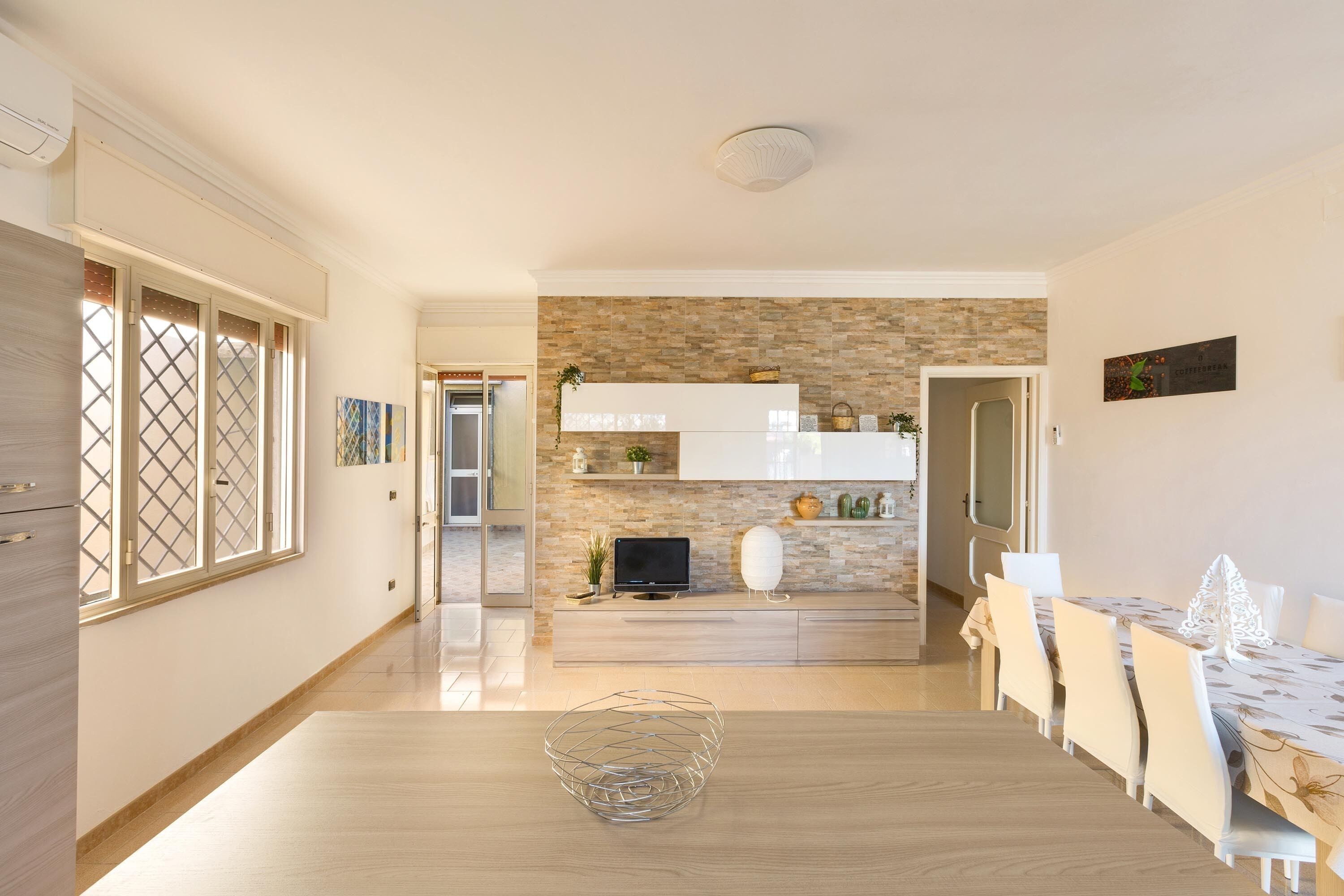 A modern kitchen with a stone backsplash, wooden cabinets, and a dining area with a table and chairs.