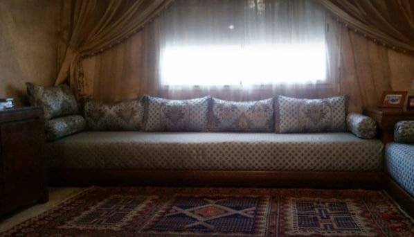 A cozy room with a sofa bed, a patterned rug, and curtains over a window. - Impeccable 2-Bed Apartment (Skhirat)