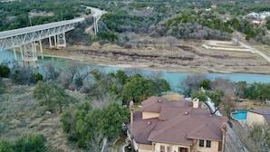 A house with a large front yard, a swimming pool, and a bridge in the background. - Luxury Lake Travis Waterfront River Retreat: pool/spa, pool table (Spicewood)