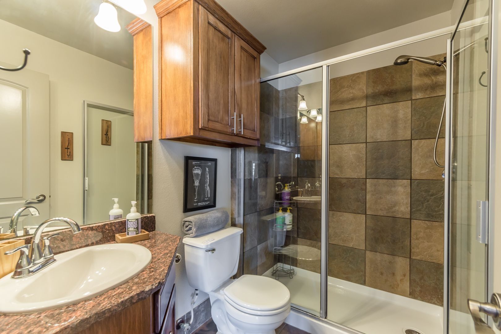 A modern bathroom with a granite countertop sink, a toilet, a glass shower enclosure, and wooden cabinets.