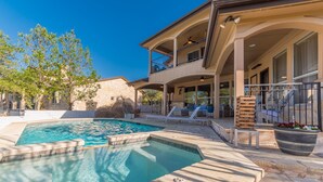 A pool area with a stone deck, lounge chairs, and a covered patio with outdoor seating. - Luxury Lake Travis Waterfront River Retreat: pool/spa, pool table (Spicewood)