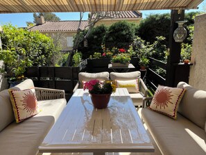 An outdoor patio with a wooden table, two beige sofas with decorative pillows, and potted plants.
