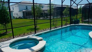A swimming pool with a hot tub, surrounded by a glass enclosure, and a view of a residential area with houses and greenery. - Brand New Home at Sonoma Resort at Tapestry (Kissimmee)