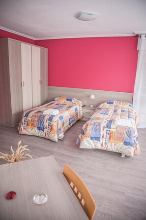 A room with two beds, a wooden wardrobe, a table, and a ceiling light. - Pensión Parque Del Ebro - Adults Only (Logroño)
