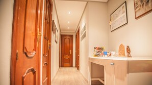 Un pasillo con puertas de madera, una consola blanca con varios objetos y cuadros en la pared.