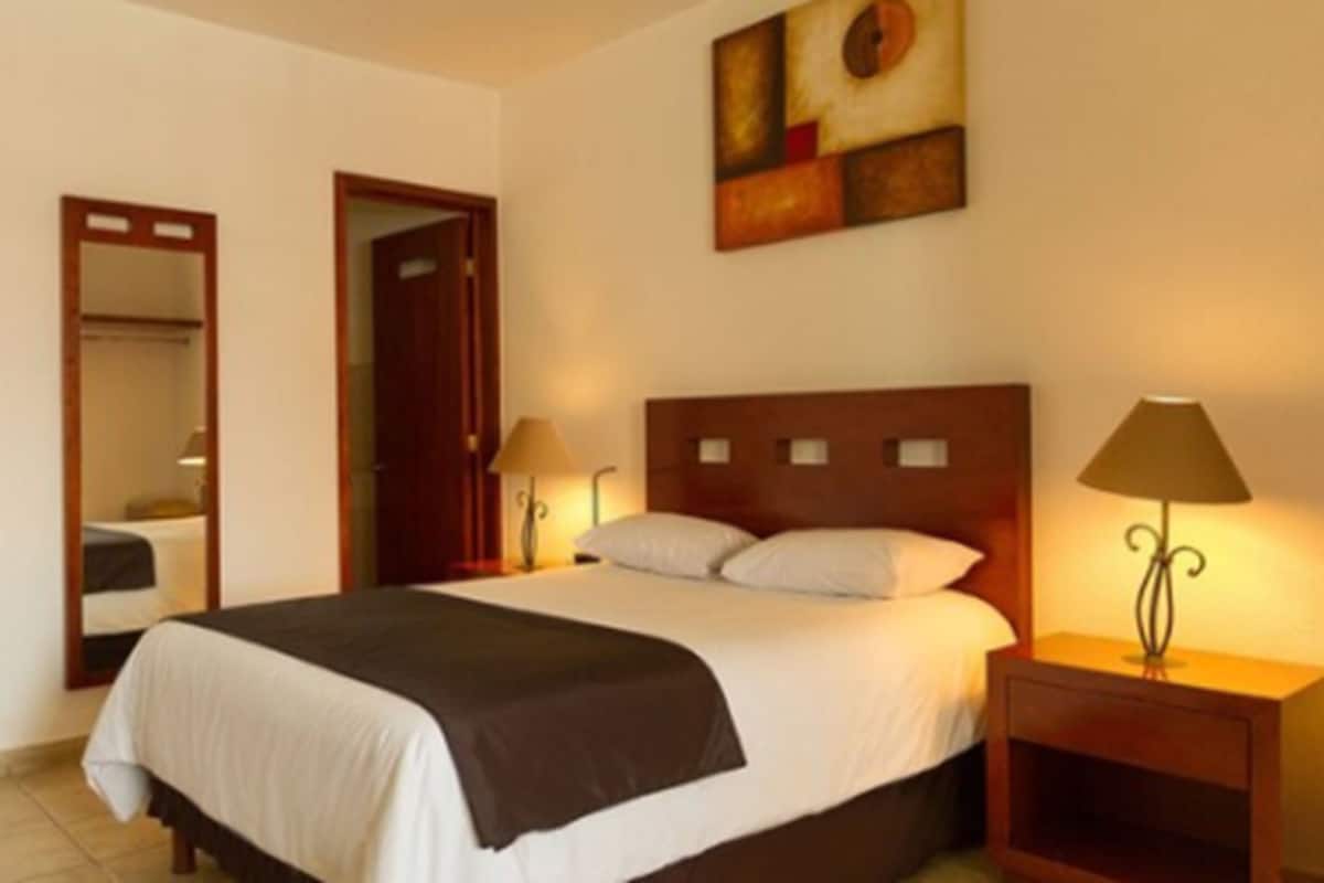 Una habitación de hotel con una cama grande, dos lámparas de noche, un espejo y un cuadro en la pared.