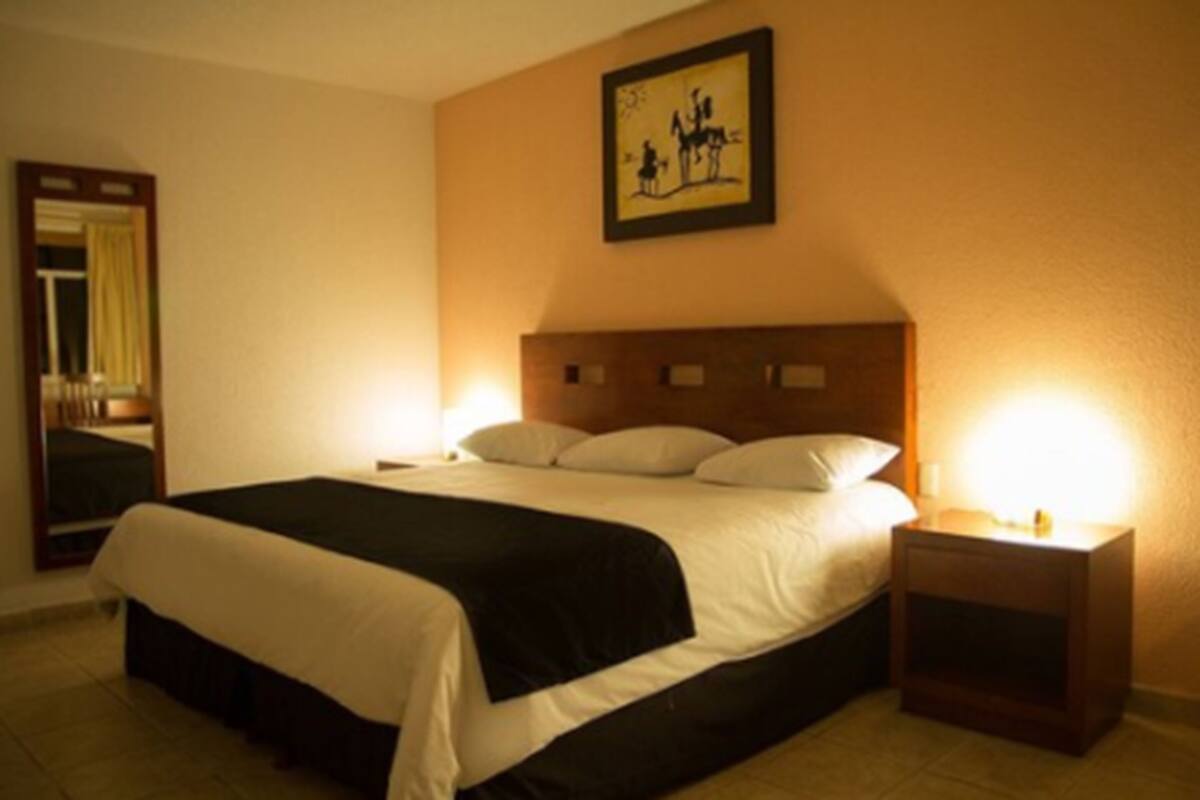Habitación de hotel con una cama grande, una mesita de noche con lámpara, un cuadro en la pared y un espejo.