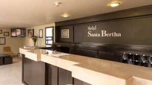 Zona de recepción de hotel con mostrador, cuadros en la pared y un cartel que dice "Hotel Santa Bertha".