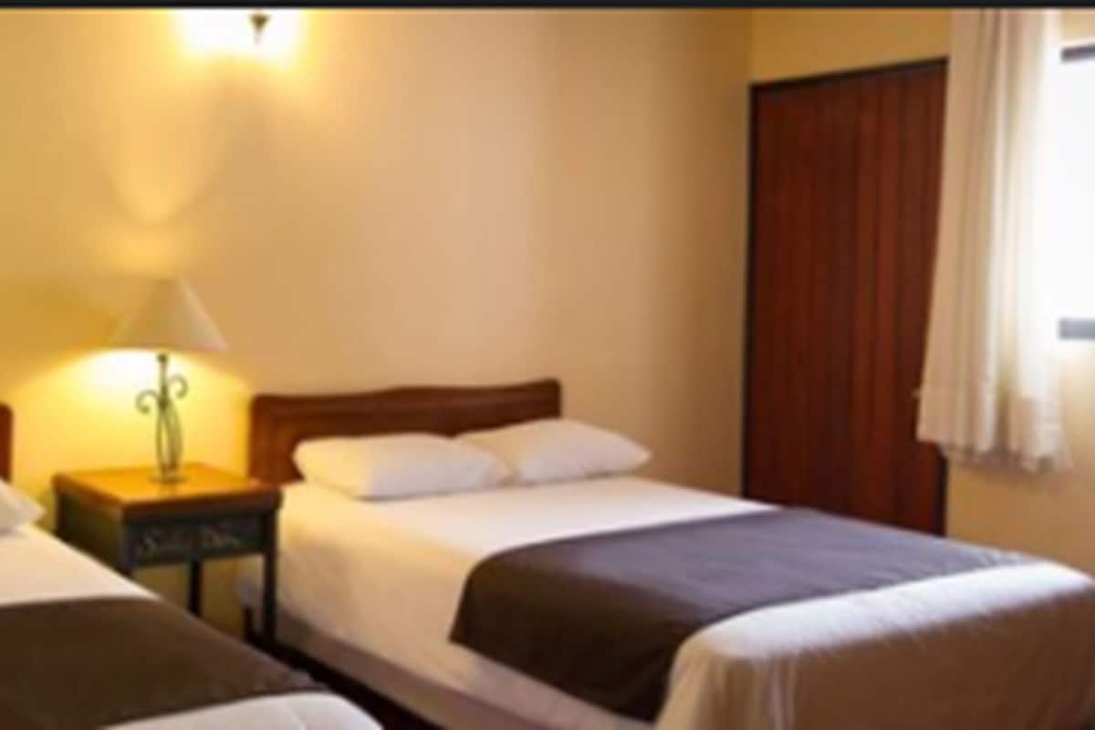 Una habitación de hotel con dos camas individuales, una mesita de noche con lámpara y una ventana con cortinas.