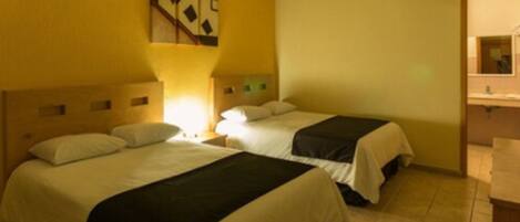 Habitación de hotel con dos camas, una mesita de noche, una lámpara y un baño visible a través de una puerta abierta.