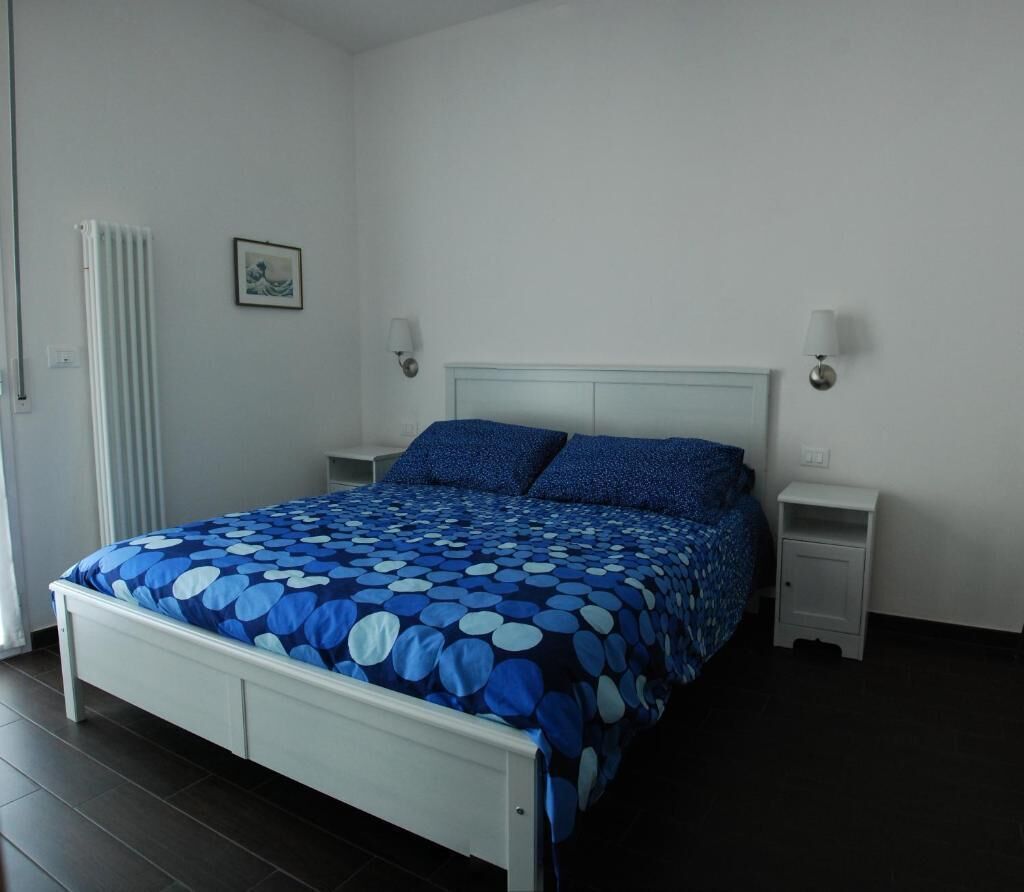 A bedroom with a bed, bedside tables, a radiator, and a wall-mounted picture.