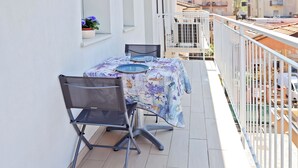 Un balcon avec une table et des chaises, un pot de fleurs et une rambarde.