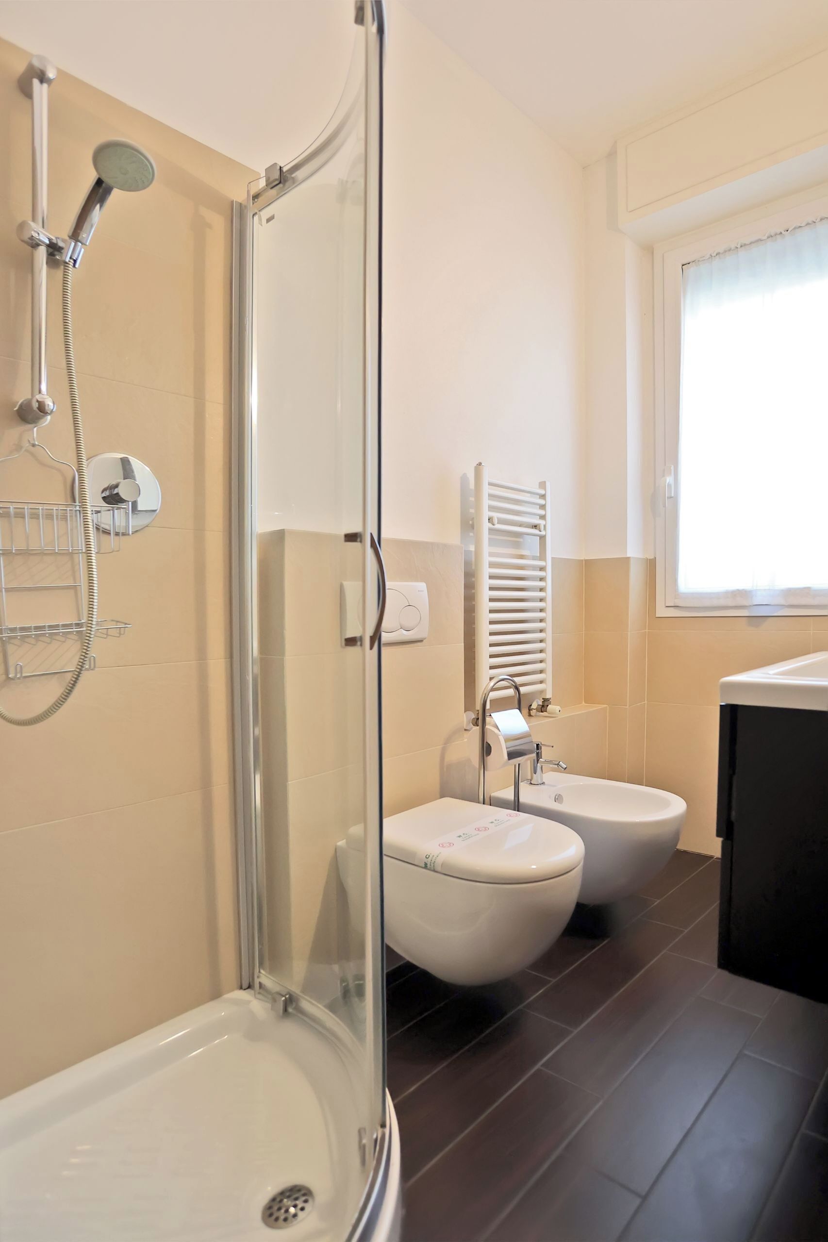 Un baño moderno con ducha de vidrio, bañera, dos inodoros y un lavamanos.