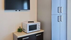 Une cuisine équipée d’un téléviseur à écran plat fixé au-dessus d’un four à micro-ondes sur un plan de travail, d’un meuble avec des tiroirs et d’un meuble bleu doté de poignées.