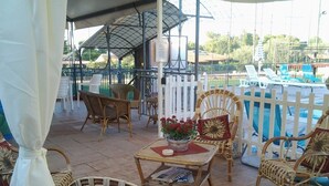 Un patio al aire libre con mobiliario de mimbre, una mesa con planta en maceta y vista a una piscina.