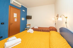 A hotel room with a yellow bedspread, a wooden door with a sign, a television mounted on the wall, and a bedside lamp.