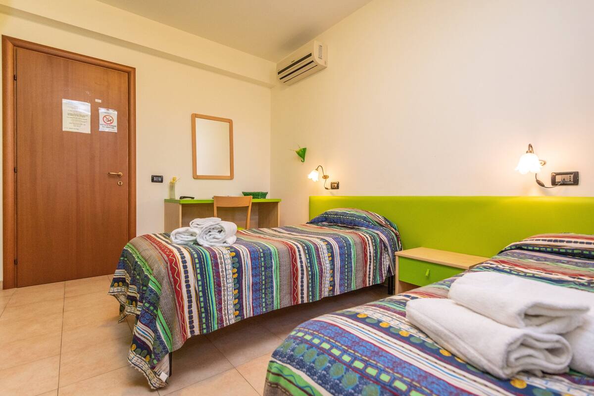 Une chambre d’hôtel avec deux lits, une porte en bois, un bureau, une chaise et un miroir.