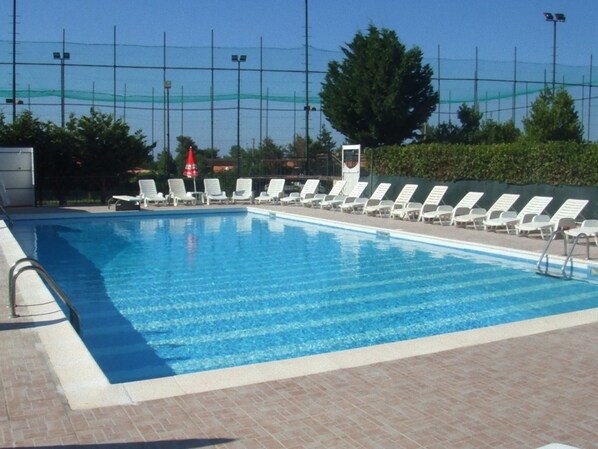 A swimming pool with white lounge chairs and a red umbrella.