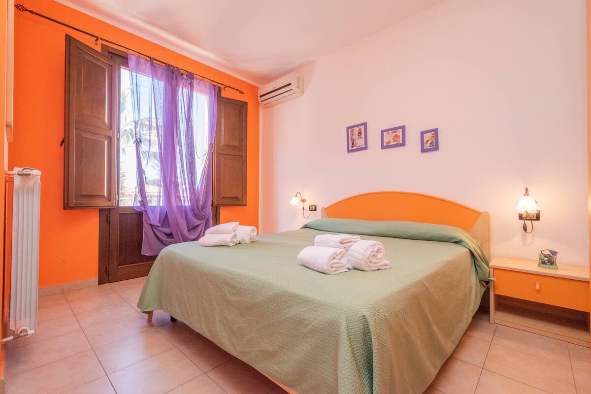 Une chambre à coucher comprenant un lit, une table de chevet, une fenêtre avec des rideaux et des lampes fixées au mur.