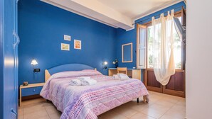 Un dormitorio con cama, lámparas de noche, mesita de noche, ventana con cortinas y vistas a palmeras.