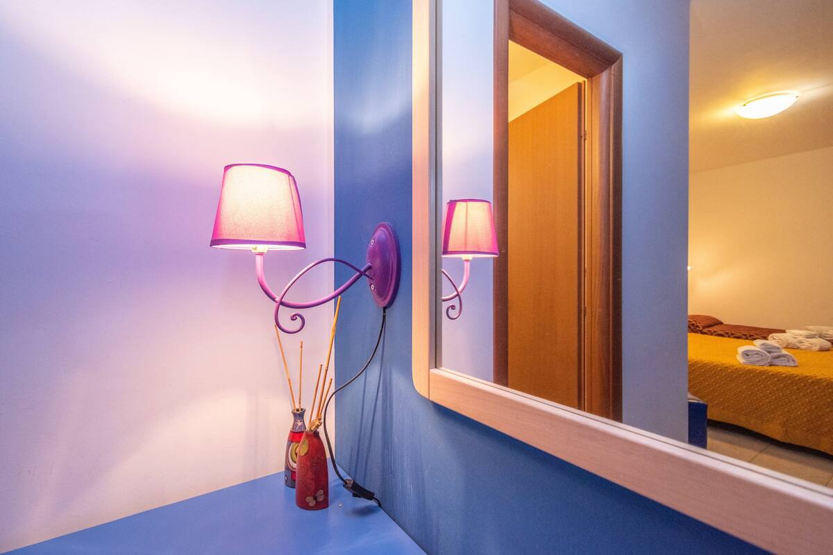 Une chambre d’hôtel avec un lit, un miroir et deux lampes fixées au mur.