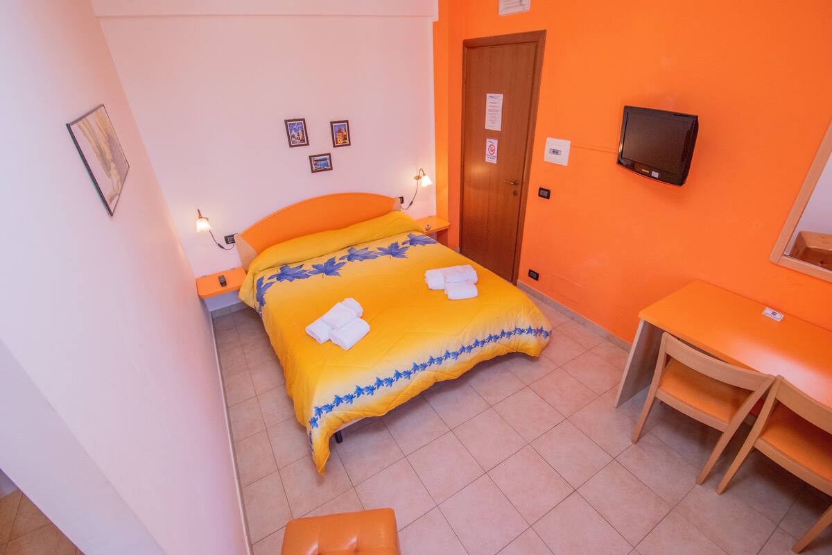 Une chambre d’hôtel avec un lit, un bureau, une chaise et un téléviseur fixé au mur.