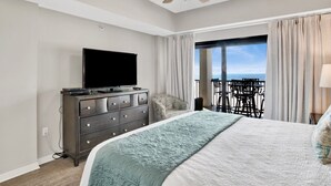 Quarto de hotel com cama, penteadeira, televisão e varanda com vista para o oceano.