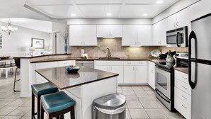 Cozinha moderna com armários brancos, bancada de granito, eletrodomésticos de aço inoxidável e uma ilha central com banquetas.