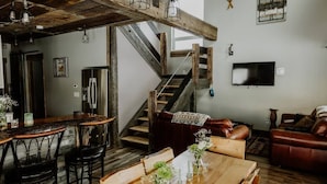 Ein rustikales Interieur mit freiliegenden Holzbalken, einer Treppe, einem Essbereich mit Holztisch und einem Ledersofa.