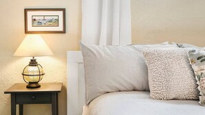 A bedroom with a bed, a bedside table with a lamp, a framed picture on the wall, and a window with curtains. - Meadowlark Apartment - 10 min to Denver, 1 hr to Mnts/skiing (Lakewood)