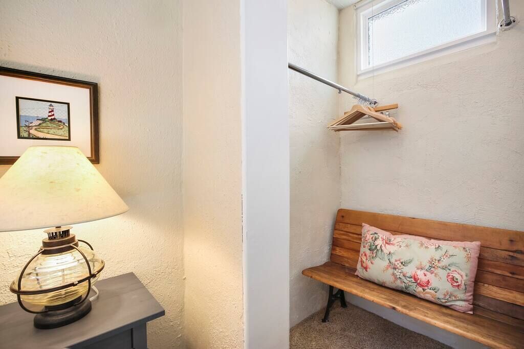 Un coin avec une lampe, un banc agrémenté d’un coussin à motifs floraux et un tableau encadré représentant un phare.