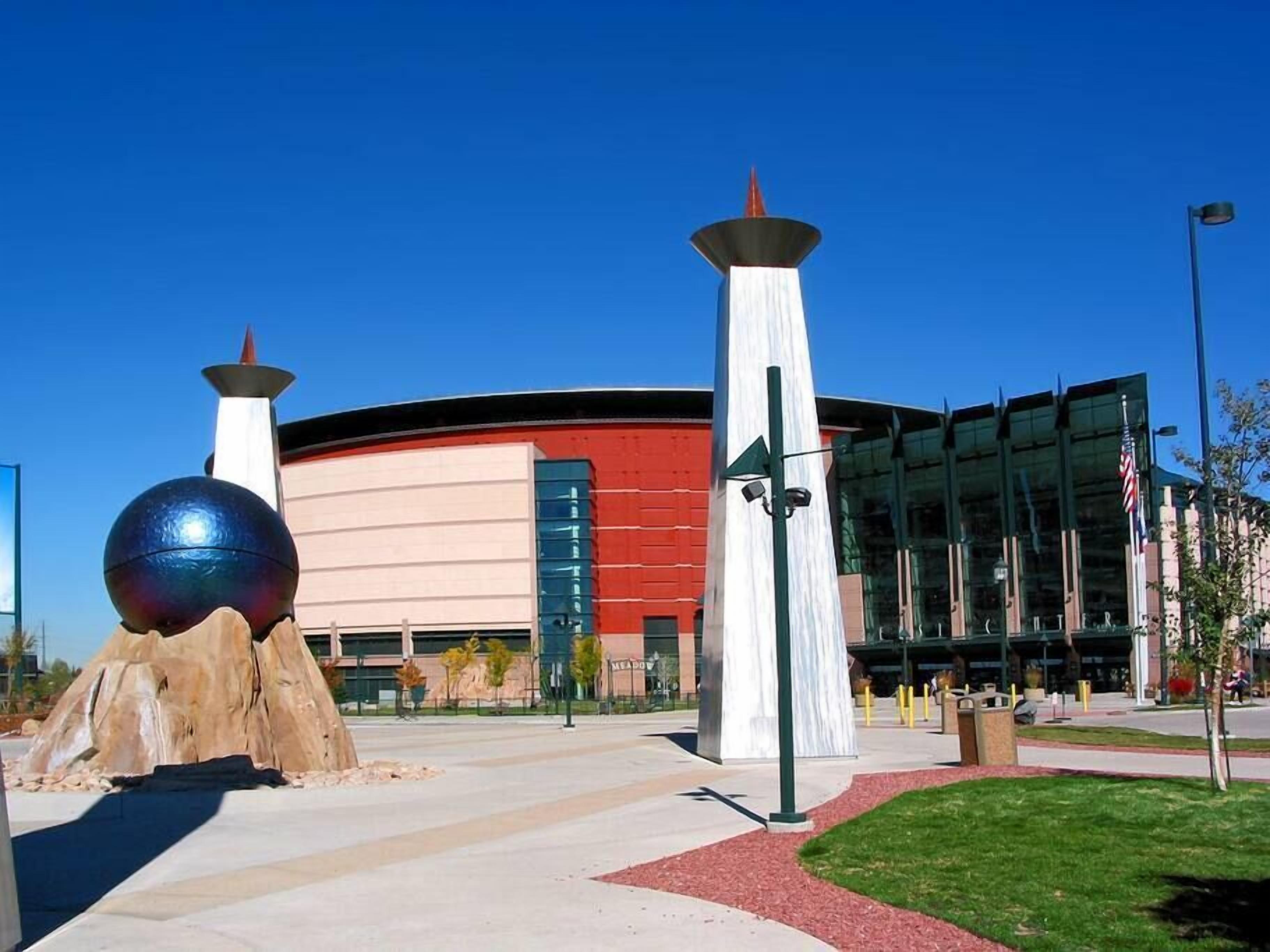 A modern building with a curved facade, large glass windows, and a prominent spherical sculpture in the foreground.