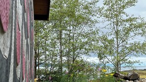 A rustic wooden structure with peeling paint, surrounded by natural vegetation and a rocky terrain.